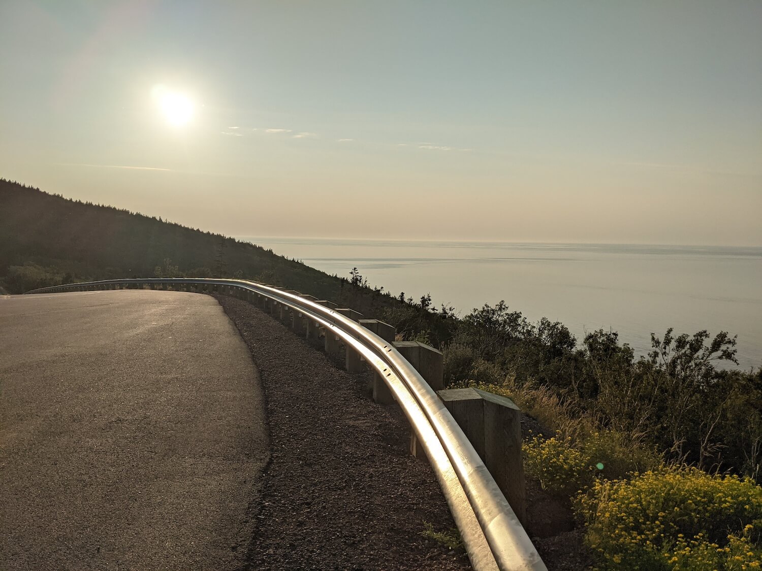 an image of a road with the ocean and sun in the background
